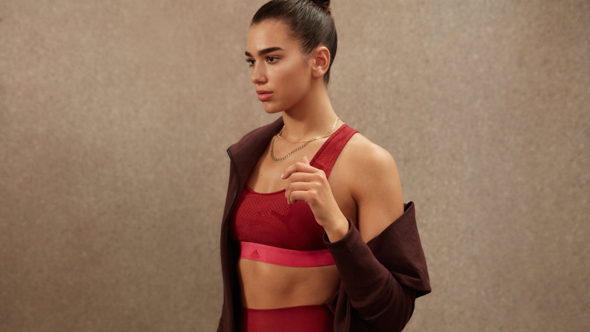 English singer Dua Lipa, brunette, in a red sports outfit and dark jacket, captured in high-resolution 8K Ultra HD for a PC desktop wallpaper.