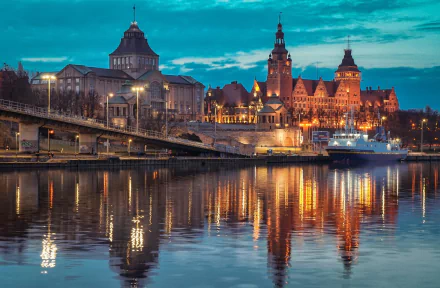 Night view of man-made architecture in Szczecin, Poland, with illuminated historic buildings reflecting on the calm water, captured as an HD desktop wallpaper background.