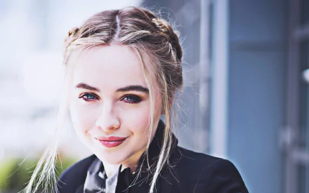 Close-up HD wallpaper of American singer Sabrina Carpenter with blonde braided hair, blue eyes, and a smile, wearing lipstick and a black outfit.