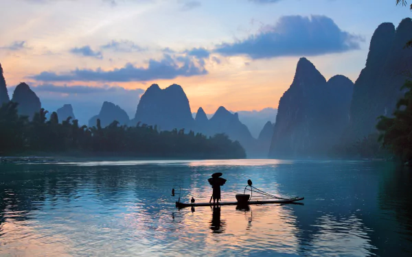 HD photography of a fisherman standing on a bamboo raft at sunrise, with misty mountains and calm water creating a serene PC desktop wallpaper background.