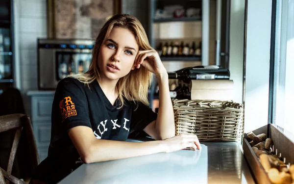 Blonde woman model with striking blue eyes sits at a bright café table, captured in sharp 4K Ultra HD quality for PC desktop wallpaper.