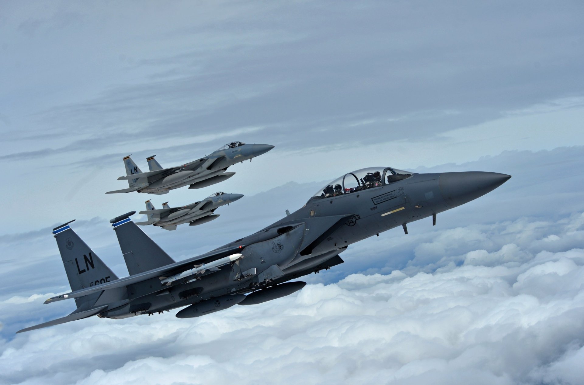 HD desktop wallpaper showing three McDonnell Douglas F-15 Eagle jet fighter warplanes flying above clouds in a clear sky, representing military aircraft.