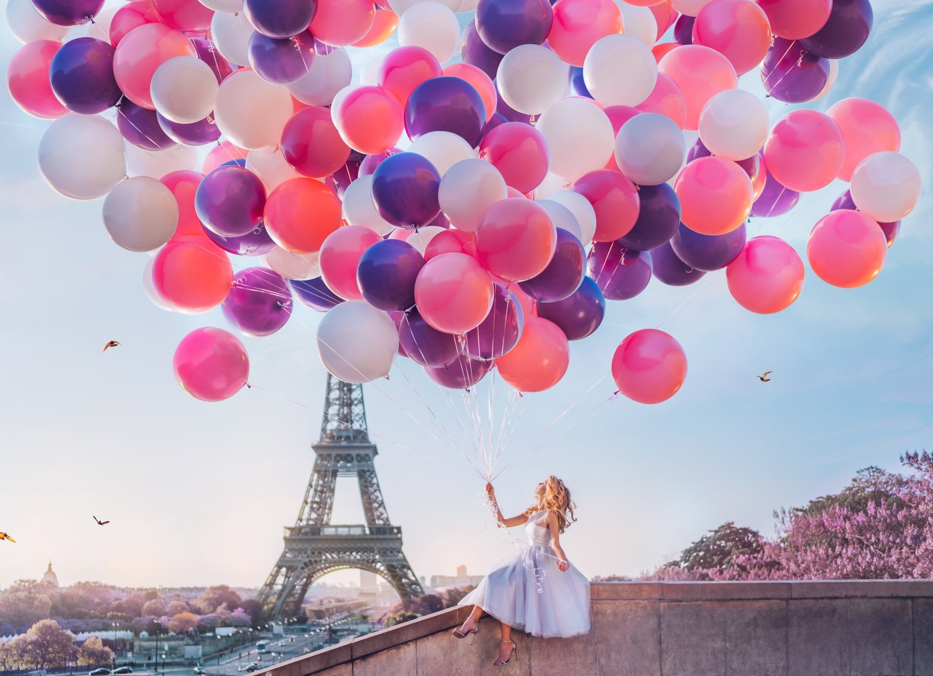 8K Ultra HD PC wallpaper/background: blonde model in a flowing white dress releasing pink and purple balloons on a Paris terrace with the Eiffel Tower at sunset, dreamy mood.