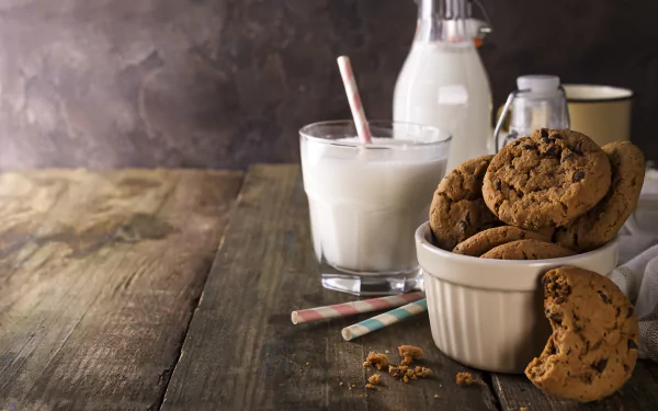 Still life food 5K Ultra HD PC desktop wallpaper: glass and bottle of milk with a bowl of chocolate-chip cookies on a rustic wooden table, crumbs scattered.
