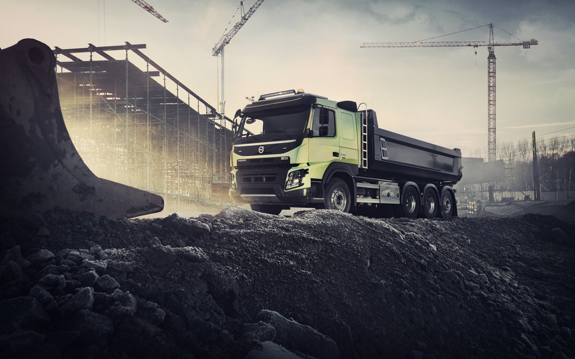 Volvo dump truck on a rugged construction site with cranes and skeletal building, dramatic lighting — 8K Ultra HD PC desktop wallpaper and background