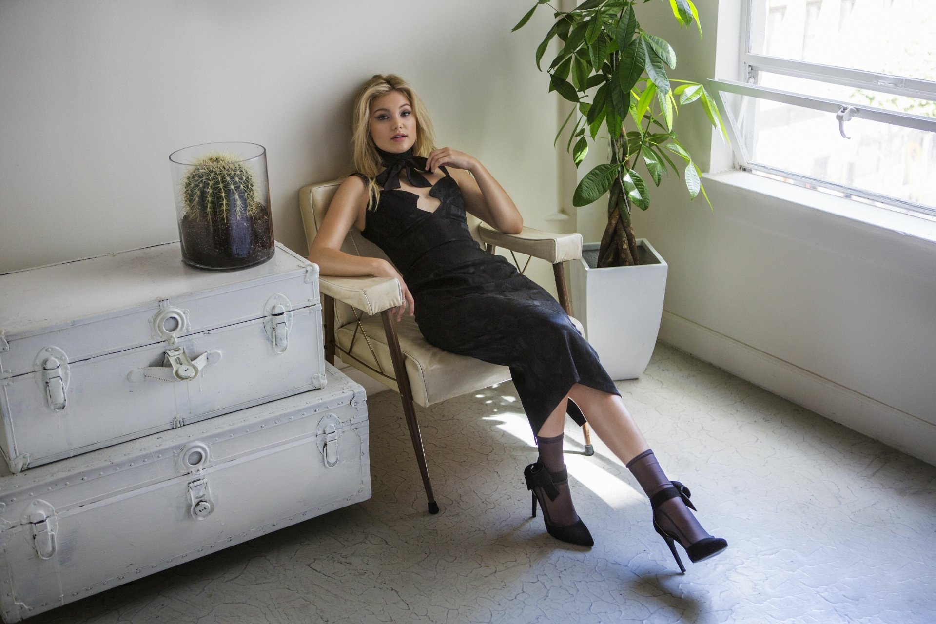 Blonde woman in a black dress and high heels lounging by a sunlit window in a minimalist studio — 5K Ultra HD PC desktop wallpaper/background.