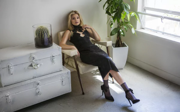 Blonde woman in a black dress and high heels lounging by a sunlit window in a minimalist studio — 5K Ultra HD PC desktop wallpaper/background.