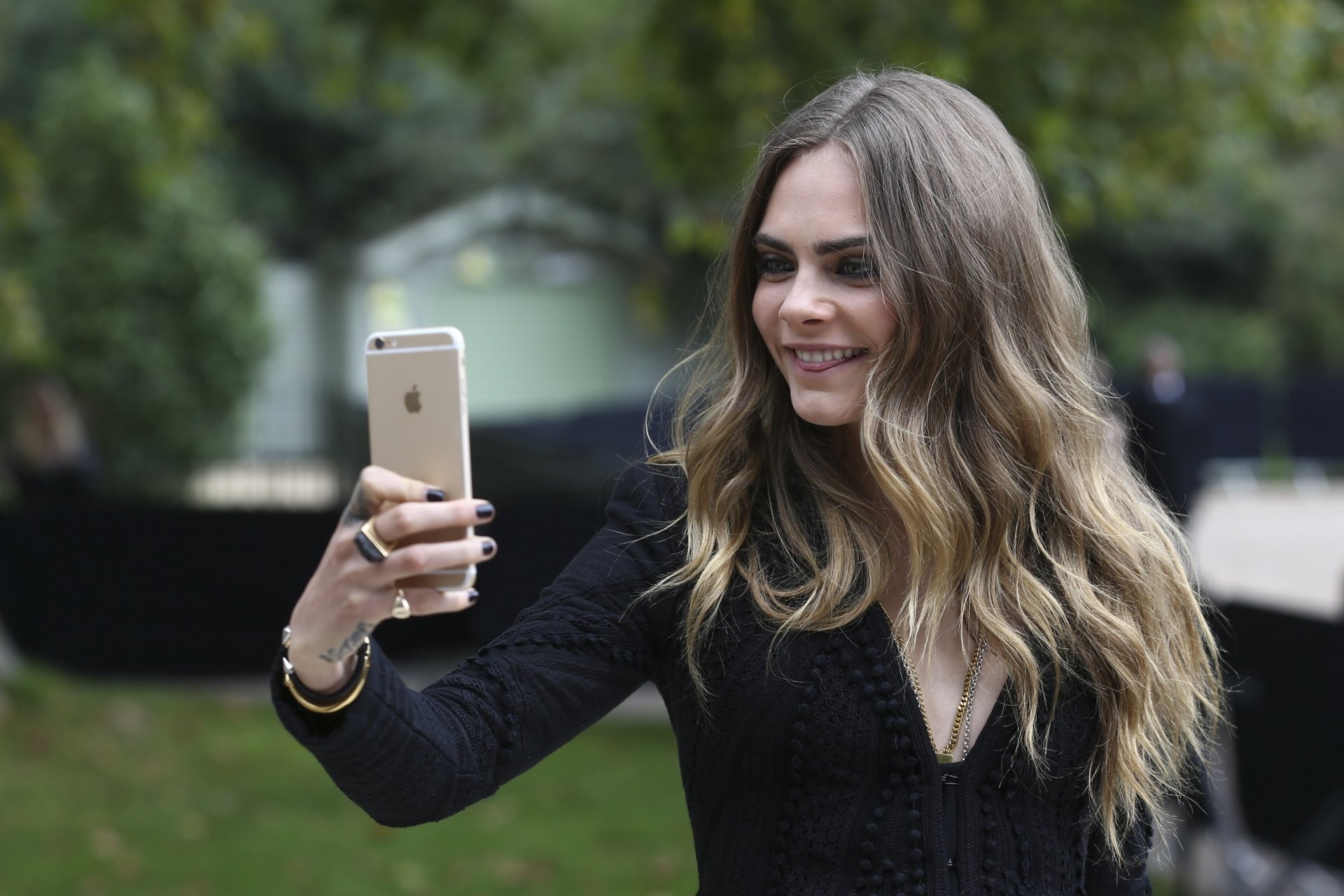 Blonde English model with long wavy hair taking a smartphone selfie, shallow depth of field, smiling portrait — 2K Quad HD PC desktop wallpaper.