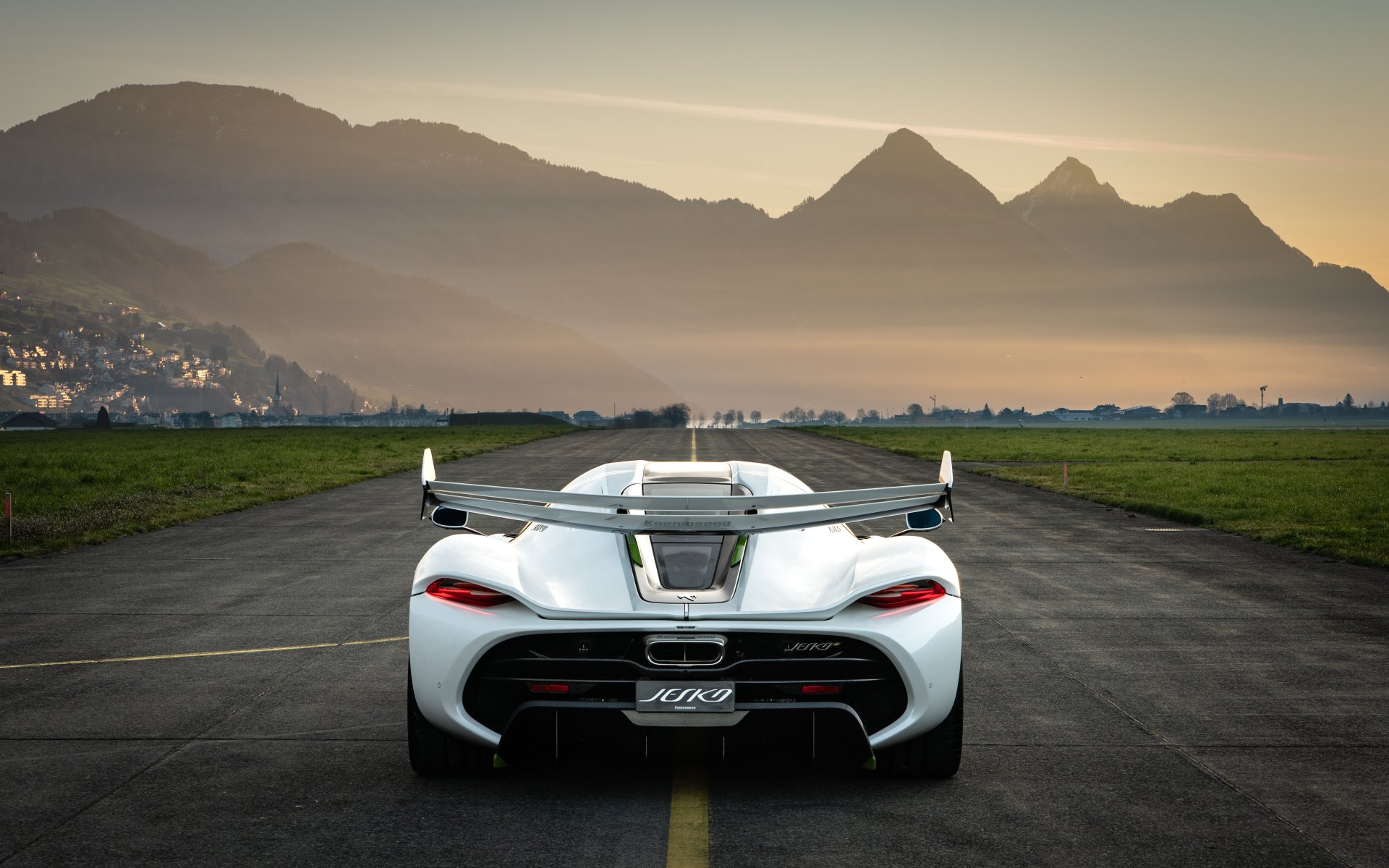 A white Koenigsegg Jesko sports car parked on a runway at sunset, with mountains in the background. 4K Ultra HD PC desktop wallpaper and background.