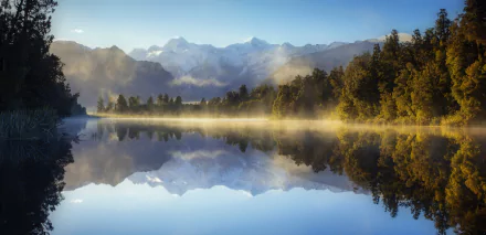 HD landscape wallpaper of a serene New Zealand lake with fog, surrounded by forest and mountains, reflecting the natural beauty in crystal-clear water.
