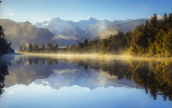 HD landscape wallpaper of a serene New Zealand lake with fog, surrounded by forest and mountains, reflecting the natural beauty in crystal-clear water.