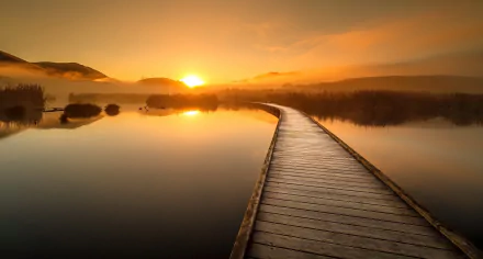 A serene sunset over a calm lake with a man-made boardwalk extending into the water, showcasing nature's beauty in this HD desktop wallpaper.