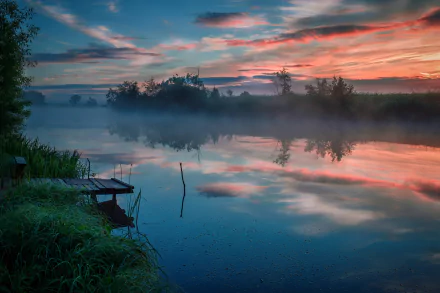 HD desktop wallpaper capturing a serene dawn over a foggy river, with calm water reflecting the colorful sky and surrounding natural landscape.