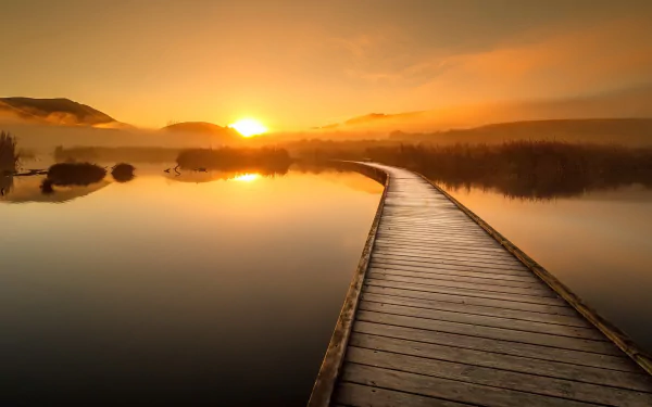 A serene sunset over a calm lake with a man-made boardwalk extending into the water, showcasing nature's beauty in this HD desktop wallpaper.