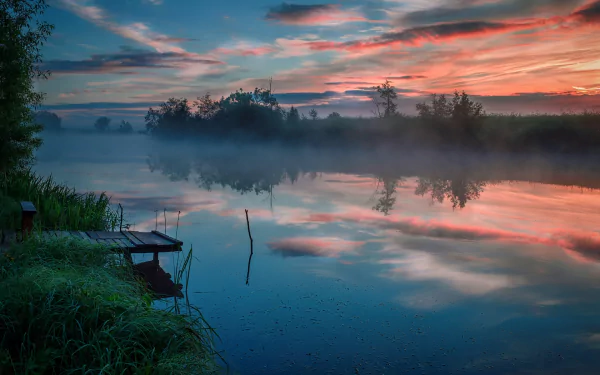 HD desktop wallpaper capturing a serene dawn over a foggy river, with calm water reflecting the colorful sky and surrounding natural landscape.