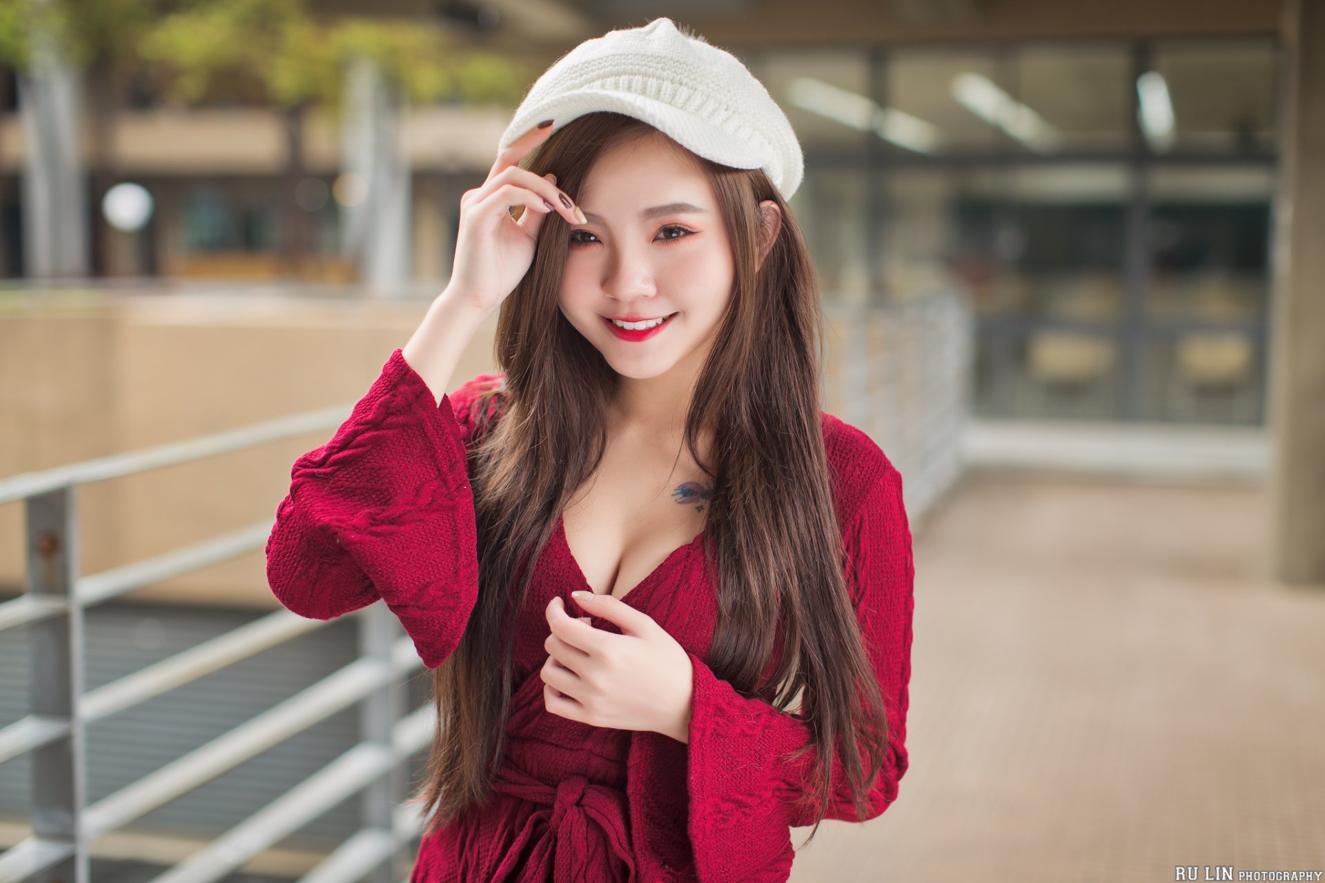 A smiling Asian woman with long brunette hair wearing a white hat and red outfit, captured with a blurred background in a high-definition desktop wallpaper.