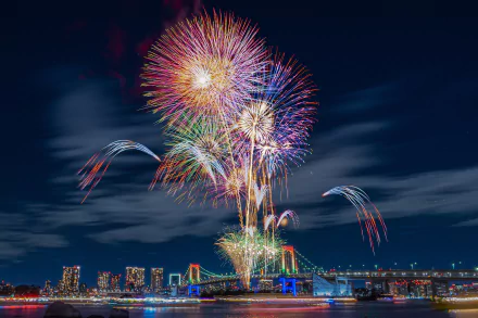 Vibrant fireworks burst over Tokyo's Rainbow Bridge at night, illuminating the city skyline in this HD desktop wallpaper capturing Japan's festive urban beauty.