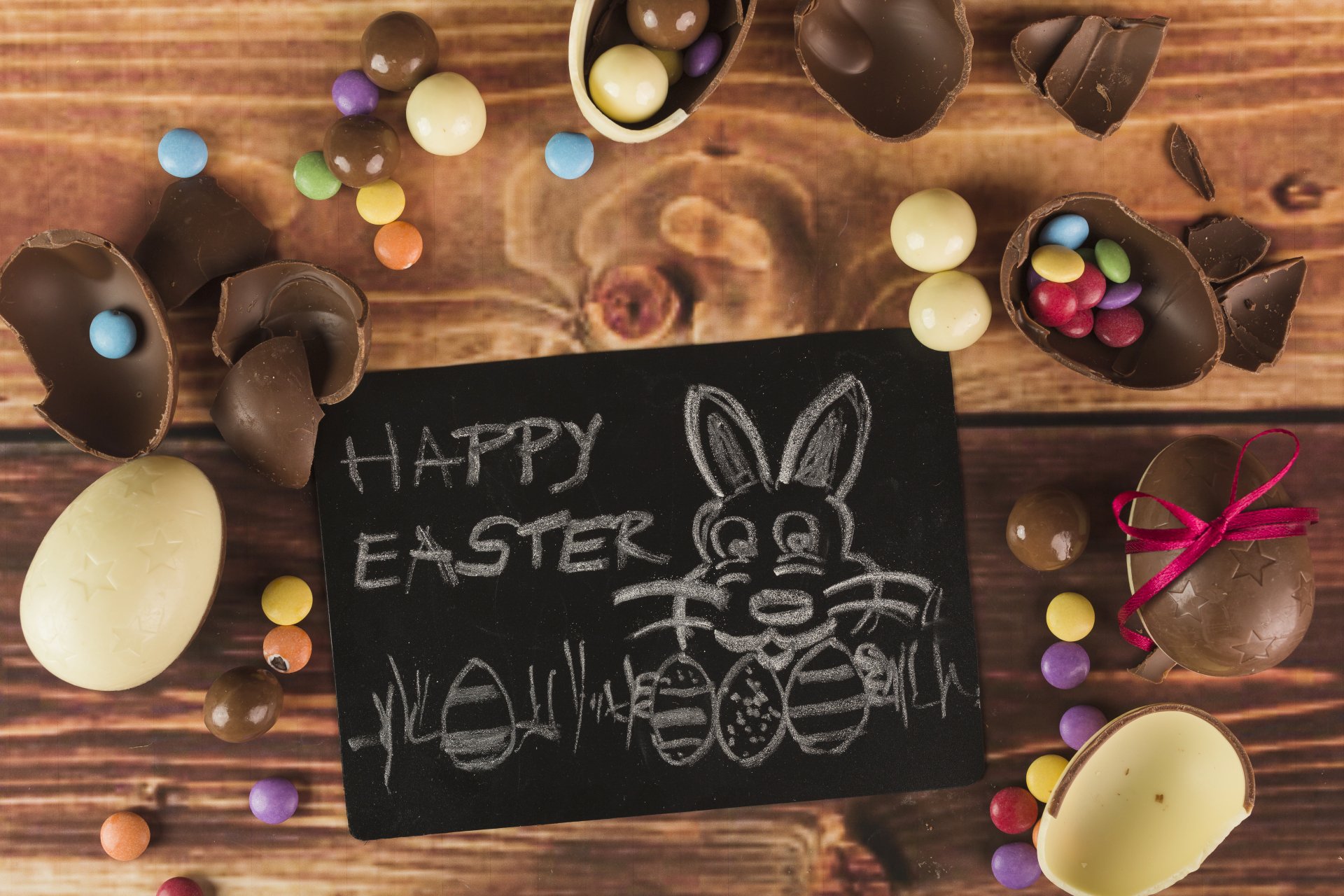4K Ultra HD Easter desktop wallpaper featuring chocolate eggs and candies surrounding a chalkboard with a bunny drawing and Happy Easter message on a wooden surface.