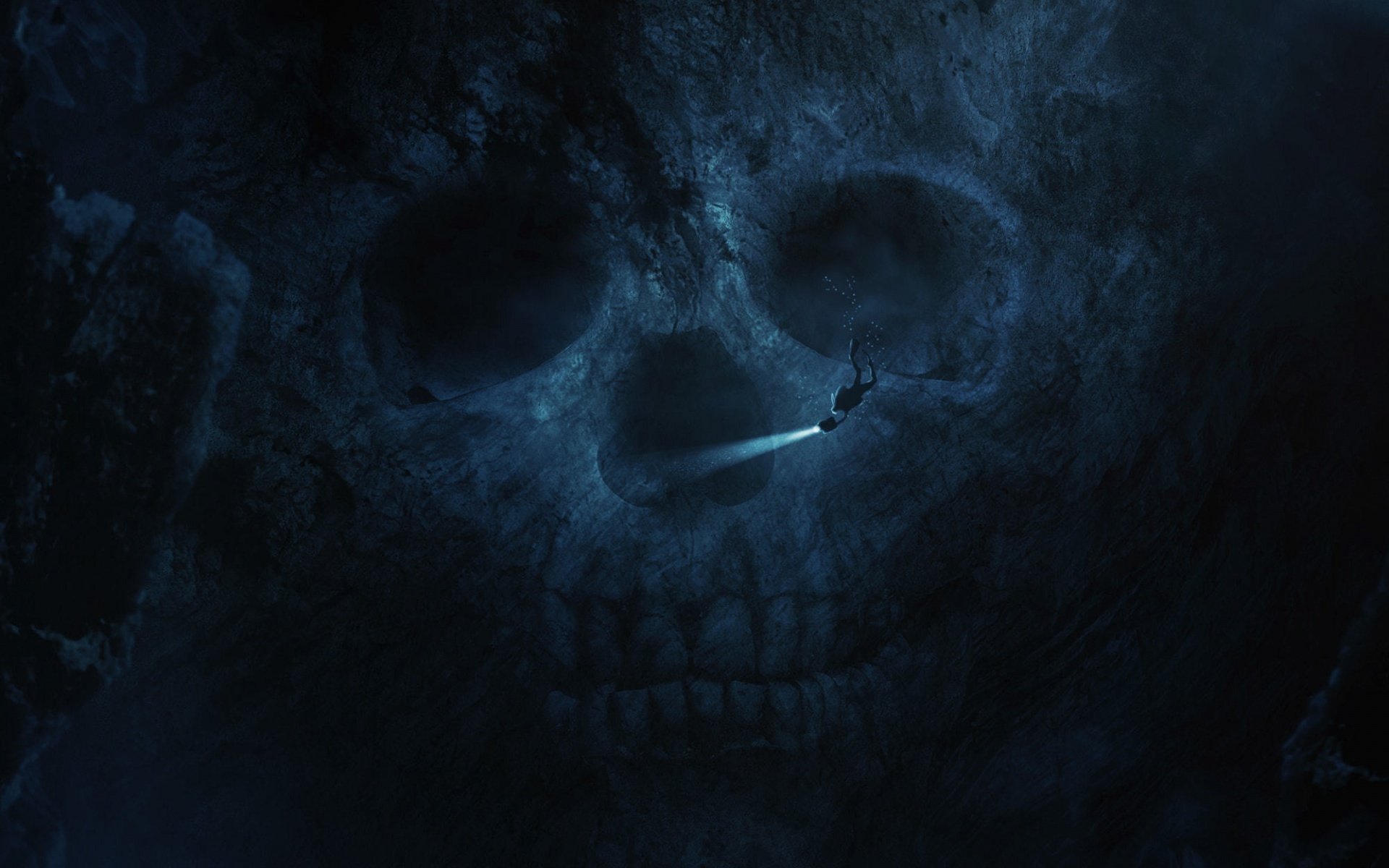 HD PC desktop wallpaper: dark underwater scene of a scuba diver swimming into the glowing eye socket of a giant submerged skull.