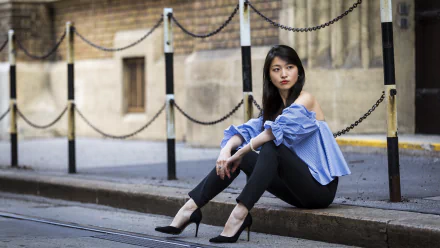 Asian woman with black hair wearing high heels and a blue off-shoulder blouse sits on a city street curb, captured in a 4K Ultra HD wallpaper-quality photo.