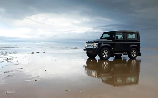 Black Land Rover Defender SUV parked on a wet reflective surface under a cloudy sky, captured in 4K Ultra HD for a striking off-road vehicle desktop wallpaper.