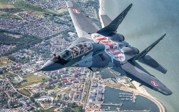HD desktop wallpaper of a Mikoyan MiG-29 jet fighter warplane banking over a coastal town, military aircraft with clear national markings.