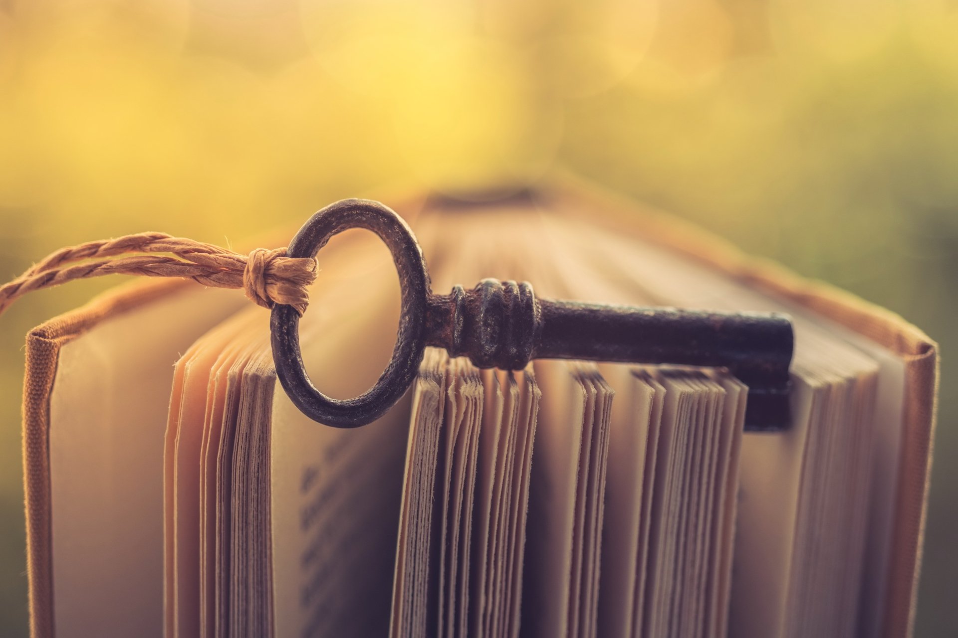4K Ultra HD PC desktop wallpaper: macro shot of an antique key resting on the open pages of a book, warm bokeh background highlighting the man-made object in soft focus.