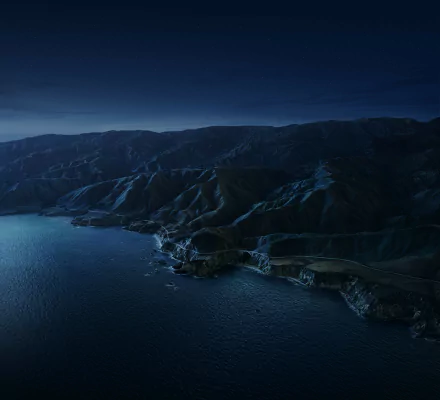 Aerial 4K Ultra HD view of Big Sur coastline at night, showcasing rugged mountains and ocean under a deep blue sky, tagged Apple Inc. desktop wallpaper.