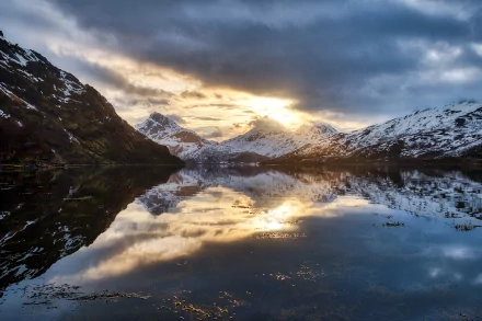 Stunning HD desktop wallpaper of Norway’s Lofoten mountains at sunset, reflecting on calm water under dramatic cloudy skies.