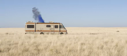 HD desktop wallpaper featuring the iconic Fleetwood Bounder RV from the TV show Breaking Bad set in a vast, dry desert landscape with smoke rising from the vehicle.