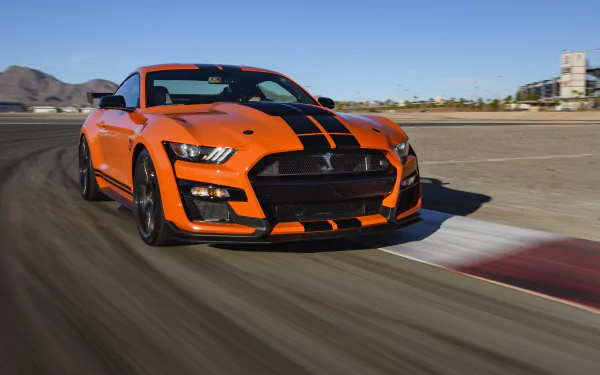 Orange Ford Mustang Shelby GT500 with black racing stripes speeding on a racetrack — 4K Ultra HD PC desktop wallpaper/background.