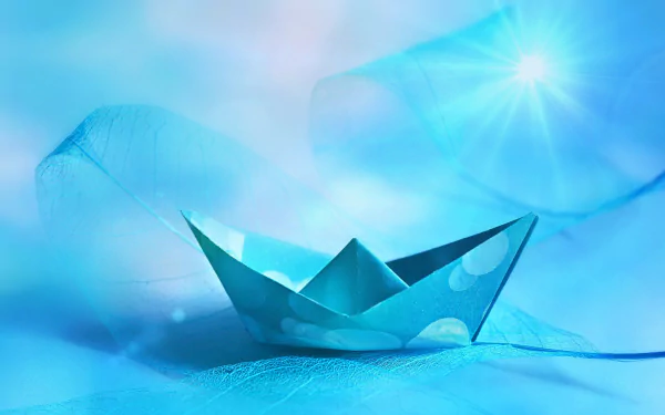 HD wallpaper of a blue origami boat on a soft, ethereal blue background, accented with a bright light flare in the top right corner.