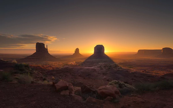 HD desktop wallpaper of Monument Valley at sunset, showcasing iconic rock formations bathed in warm, natural light against a serene sky.