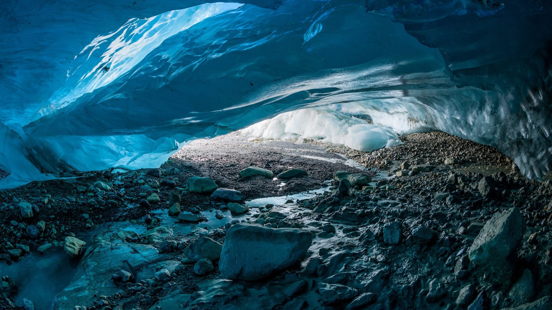 4K Ultra HD PC desktop wallpaper of an icy winter cave — blue ice ceiling, stone-strewn floor and light filtering through, dramatic natural scene.