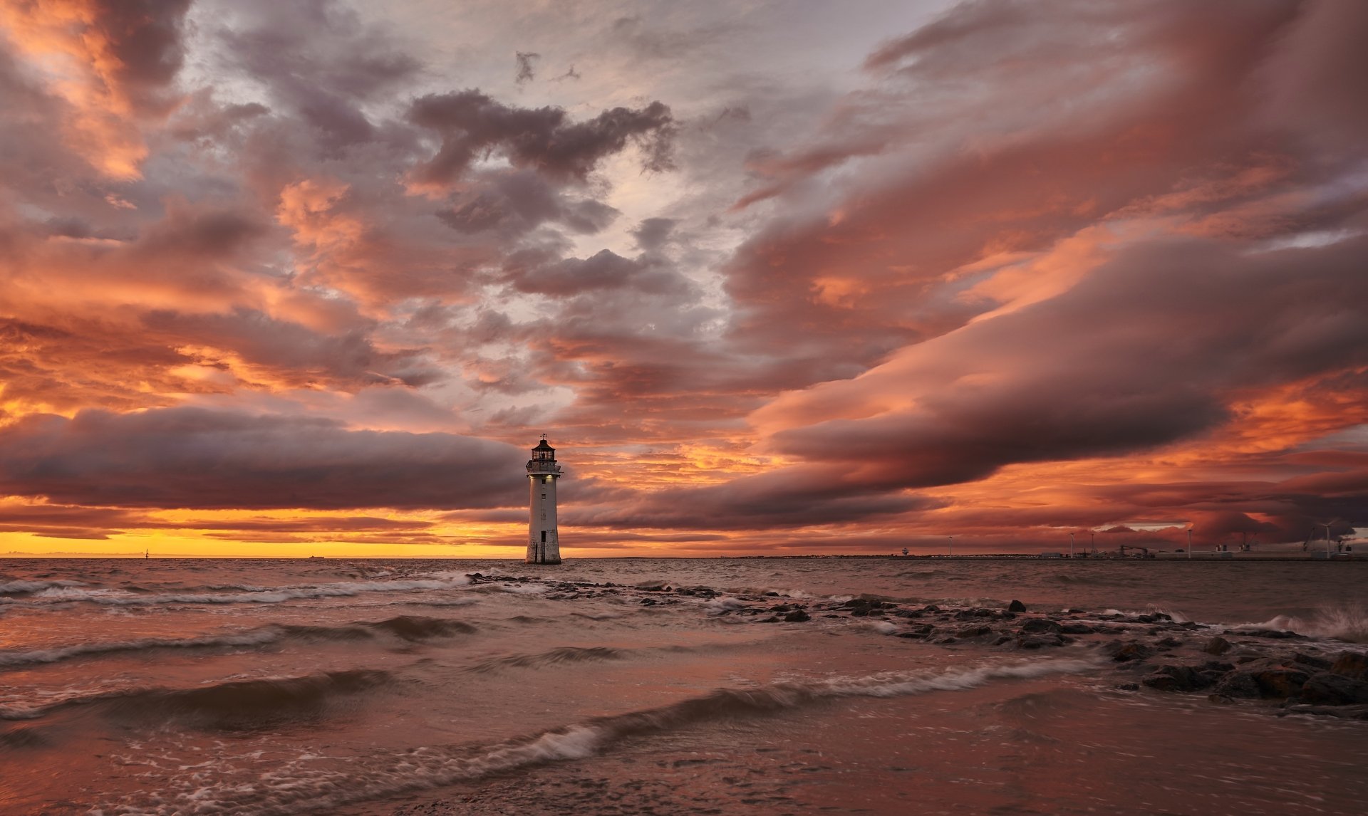 4K Ultra HD PC desktop background: solitary man-made lighthouse on a rocky shore at sunset, dramatic clouds and golden light over the sea.
