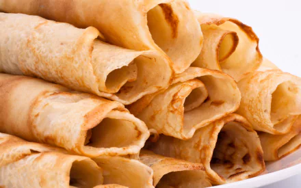 HD desktop wallpaper featuring a close-up view of freshly baked crêpes, stacked neatly on a plate. The golden-brown crêpes highlight the delicious art of baking.