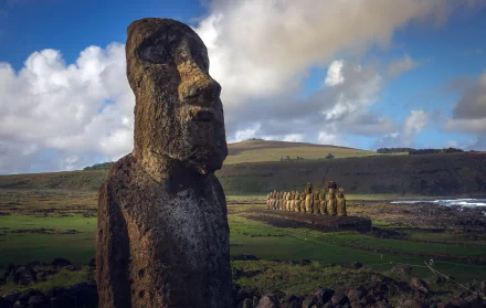 HD wallpaper of Rapa Nui's iconic man-made Moai statues on Easter Island, part of Chile's protectorate, set against a dramatic sky and rolling hills.