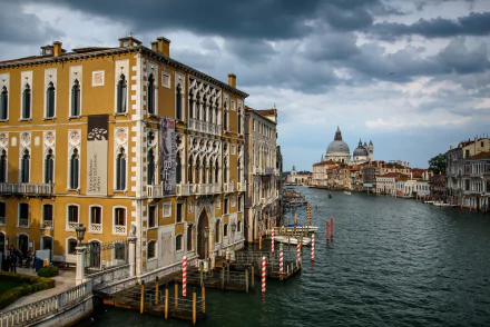 Grand Canal, Venice, Italy with a yellow palazzo at left and the domed Cathedral Santa Maria della Salute across the water beneath brooding clouds — 2K Quad HD PC desktop wallpaper background.