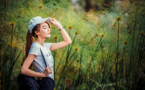 4K Ultra HD desktop wallpaper: portrait of a woman in a cap with a serene mood and model-like pose among tall green reeds.