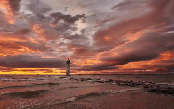 4K Ultra HD PC desktop background: solitary man-made lighthouse on a rocky shore at sunset, dramatic clouds and golden light over the sea.