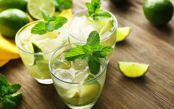 HD desktop wallpaper featuring refreshing mojito cocktails in glasses garnished with mint leaves and lime wedges on a wooden surface.