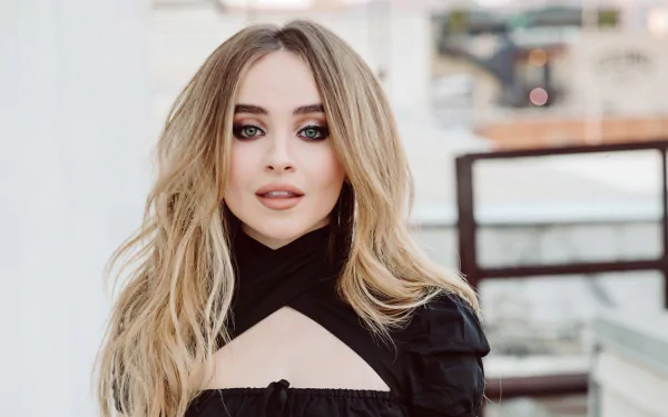 4K Ultra HD PC desktop wallpaper: close-up portrait of a blonde woman with blue eyes, smoky makeup and long waves, wearing a black cutout top against a blurred urban background.