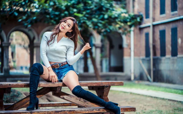 A brunette Asian woman model in shorts and knee-high boots sits on a wooden bench outdoors, captured with a shallow depth of field in 4K Ultra HD quality.