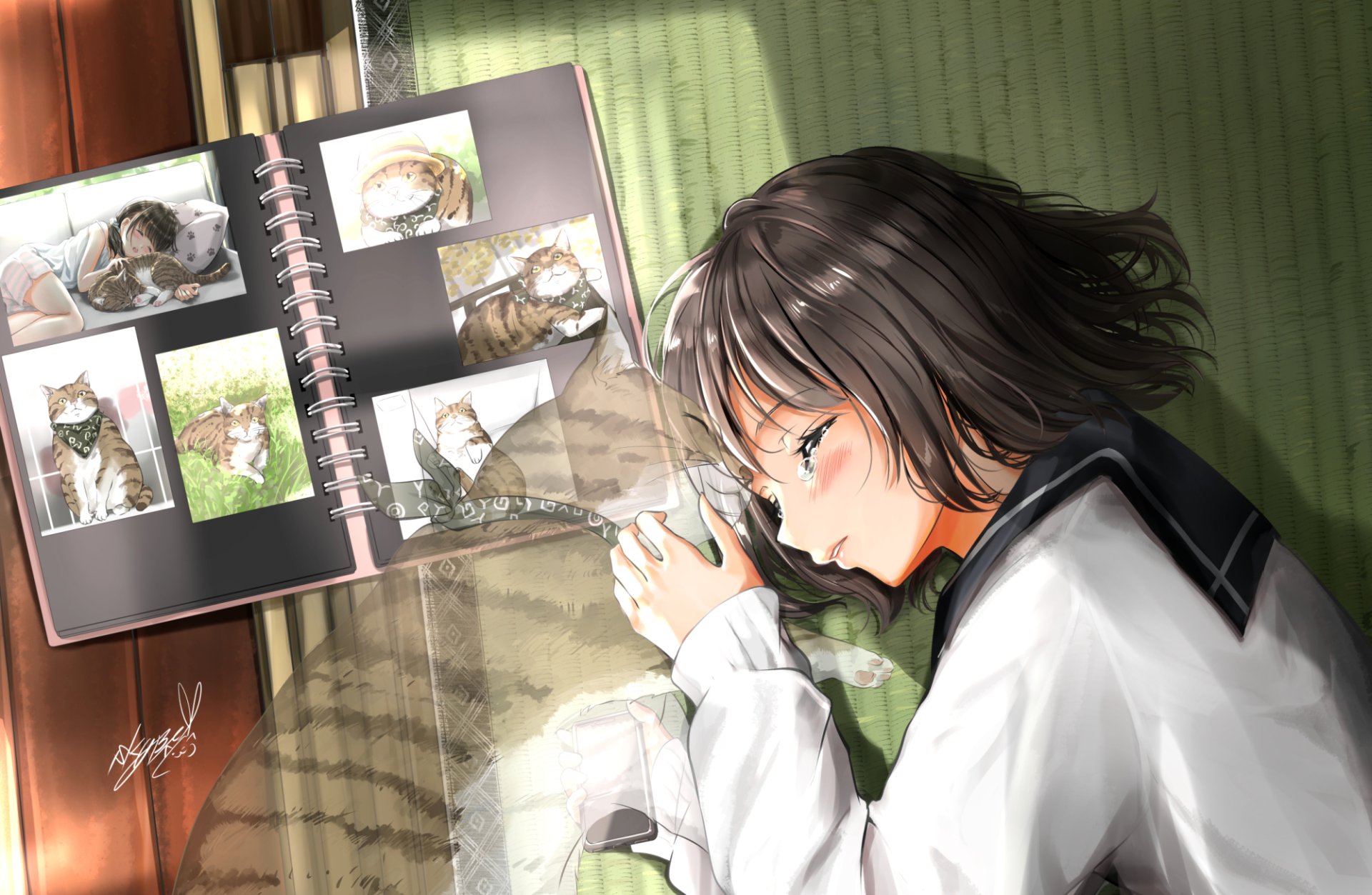 Anime girl with short black hair lying on a green surface, gently holding a cat, beside an open photo album featuring pictures of the cat in a serene HD desktop wallpaper.