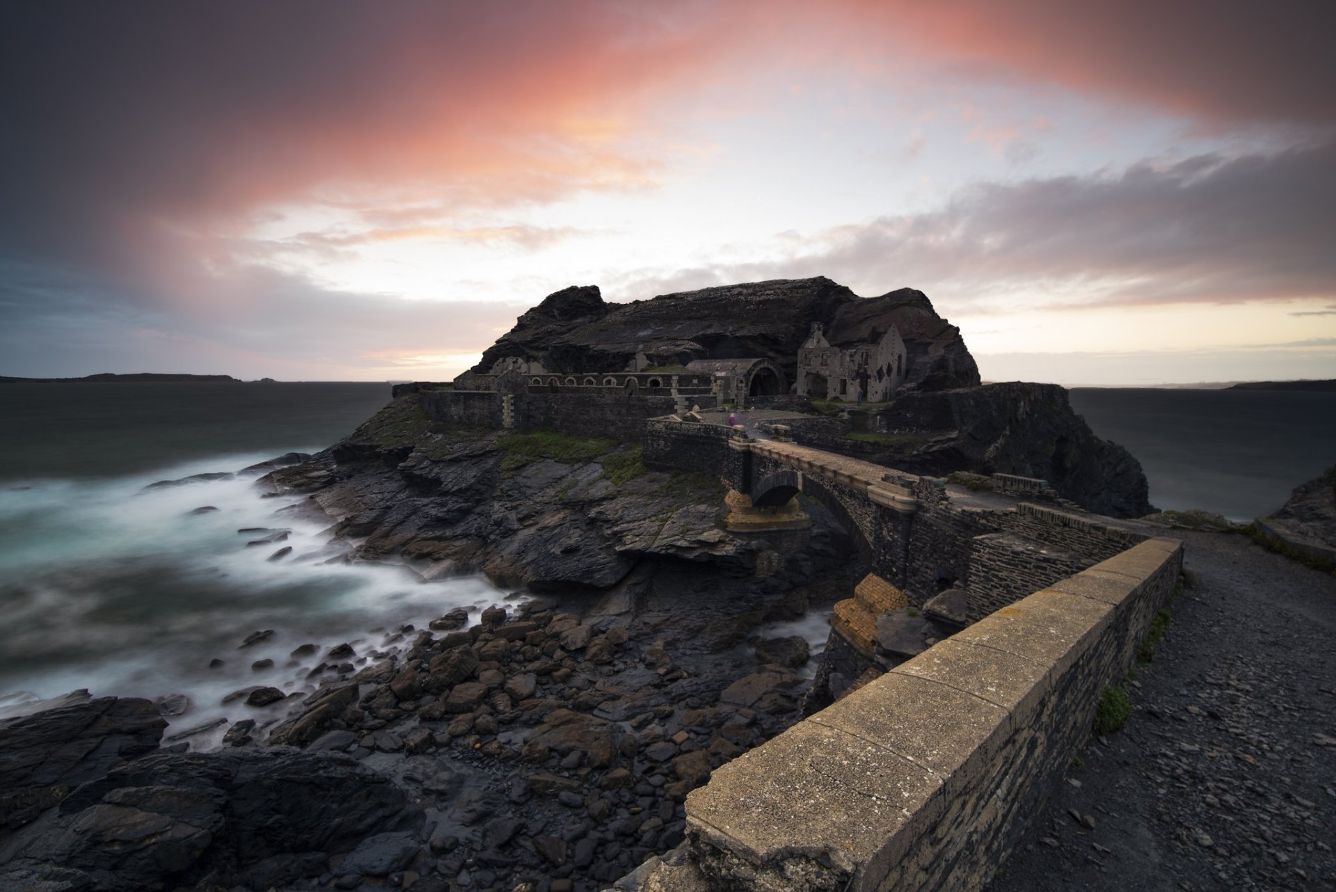 Sunset over a ruined coastal fort and man-made stone bridge at Saint-Malo, Brittany, France — rocky shore and moody skies, HD desktop wallpaper.