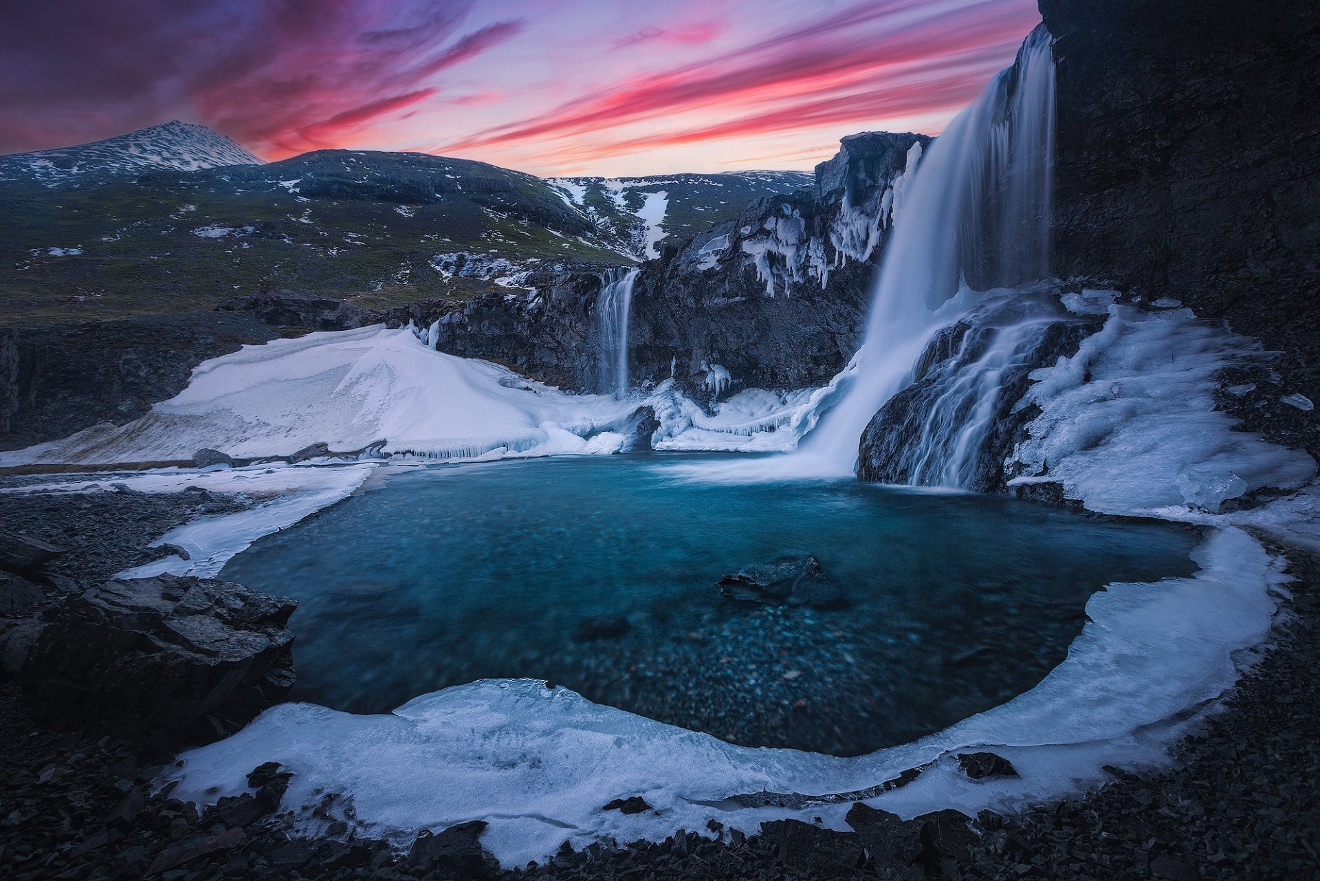 Skógafoss waterfall in Iceland at sunset, surrounded by icy river and snow-covered mountains, captured in a vibrant HD desktop wallpaper.