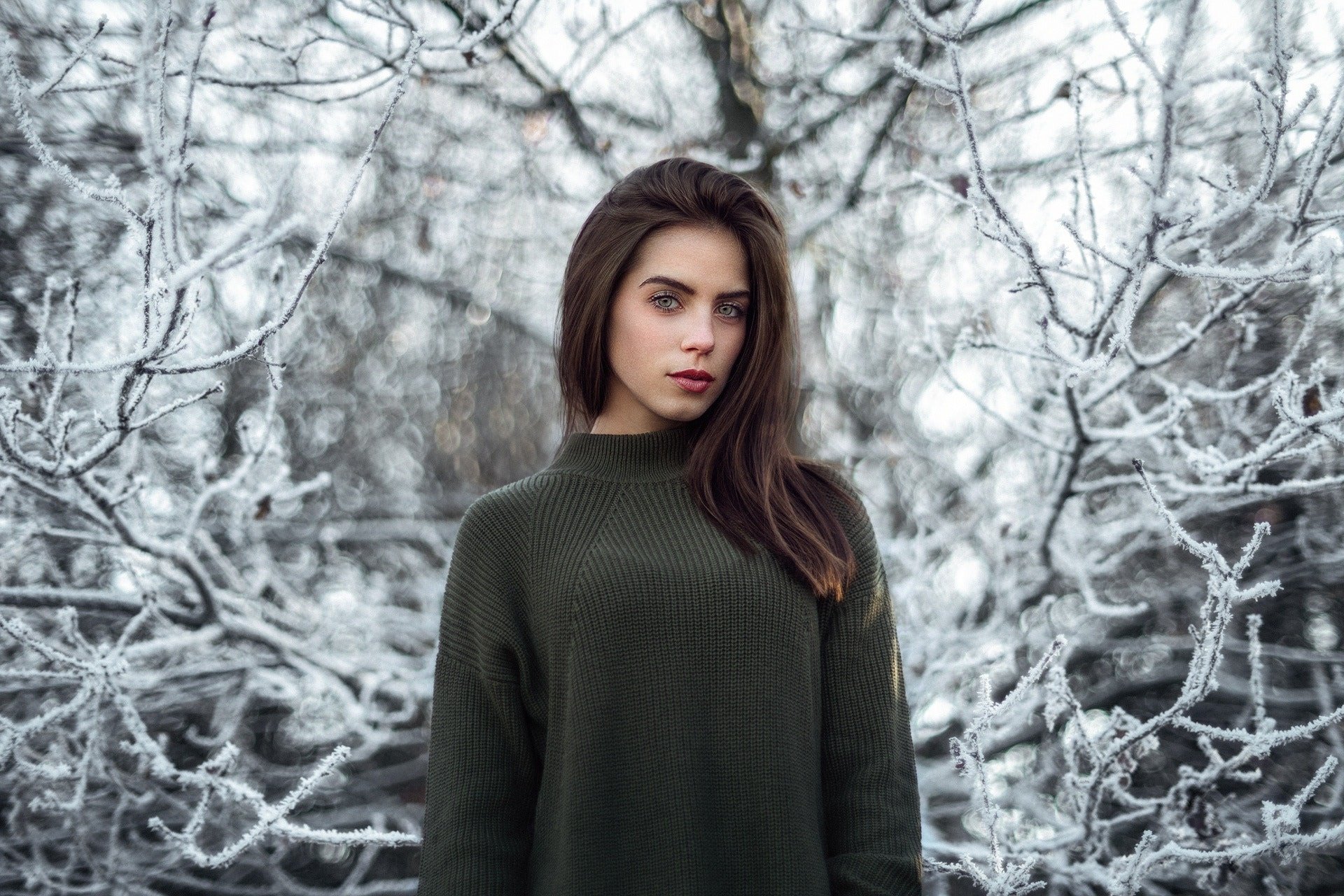 Brunette woman wearing a dark green sweater stands against a snowy winter background, captured in an HD PC desktop wallpaper by Marlen Valderrama Alvaréz.