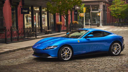 A blue Ferrari Roma sports car parked on a cobblestone street in an urban setting, featured as a high-definition PC desktop wallpaper and background.