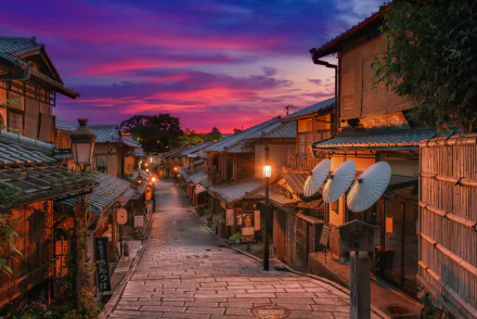 Evening view of a traditional street lined with wooden houses in Kyoto, Japan, under a vibrant pink and purple sky.