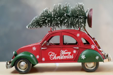 4K Ultra HD PC wallpaper of a decorative red toy Christmas car reading Merry Christmas, carrying a snowy Christmas tree on its roof, holiday snowflake accents.